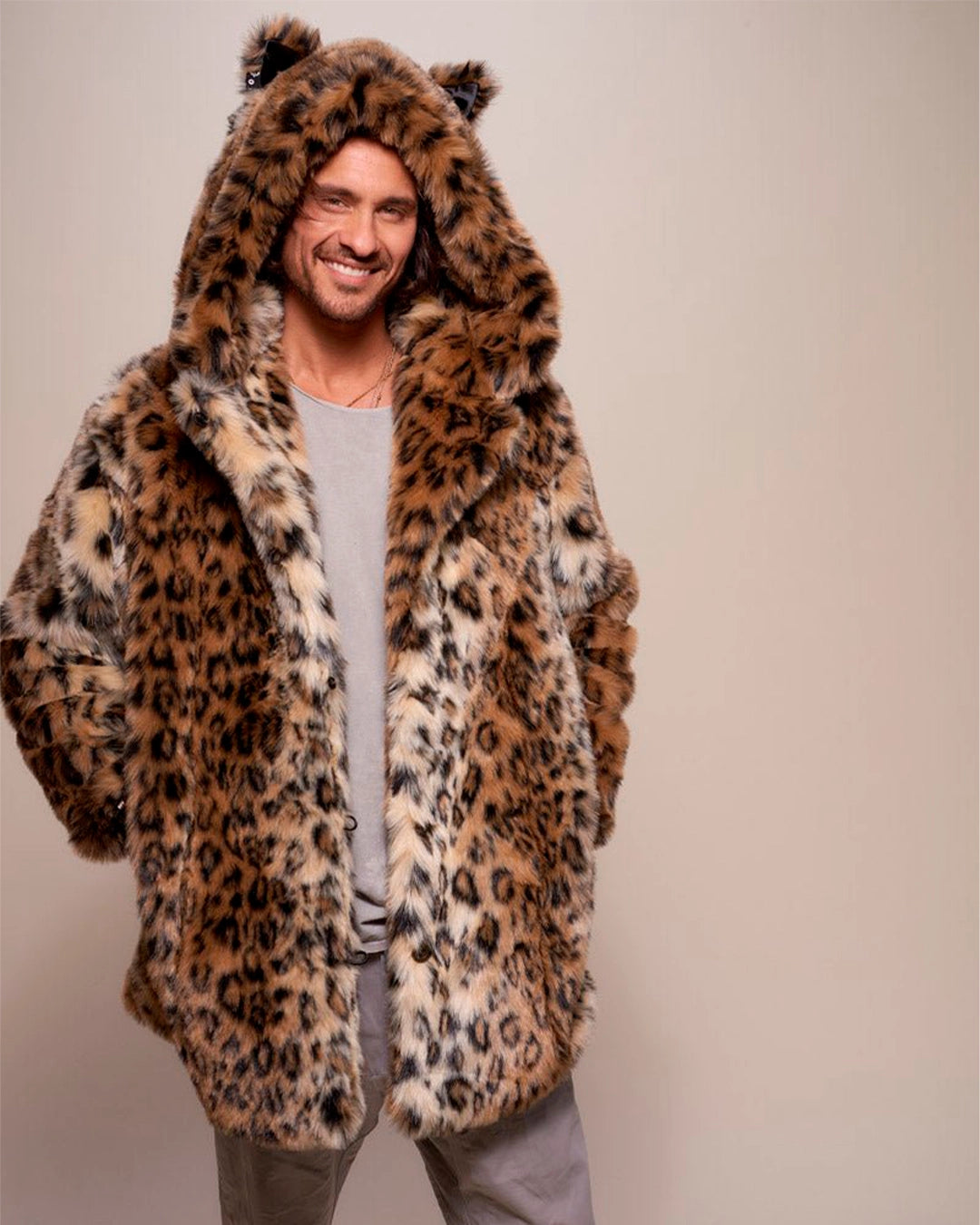 A Man wearing a leopard print fake fur jacket with an oversized hood adorned with feline ears, with his hands in the two outer coat pockets on a plain background. SpiritHoods Made To Order Leopard Print Fake Fur Coat for Men