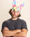 Man wearing colorful fake fur bunny ears against a beige background