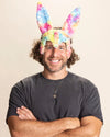 Man wearing colorful tie-dye bunny ears in rainbow faux fur bunny mask against a beige background
