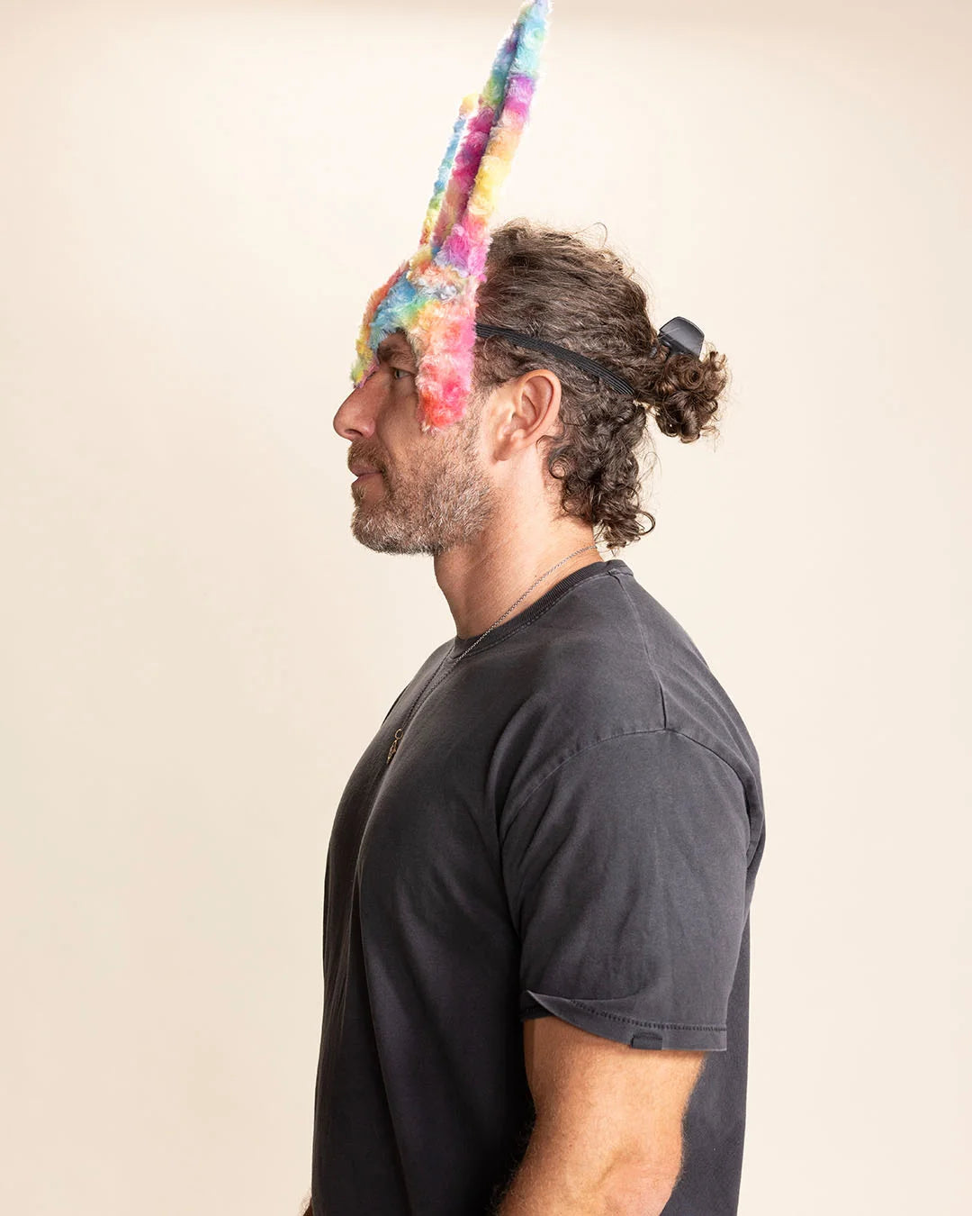 Man wearing a colorful tie-dye fake fur bunny ear mask against a plain background