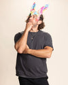 Man wearing a dark gray t-shirt and colorful  rainbow bunny ear mask against a beige background