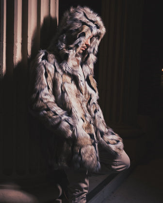 A man in the shadows, leaning against a pillar with one hand in his pocket, wearing a realistic fur Hooded Wolverine Coat.