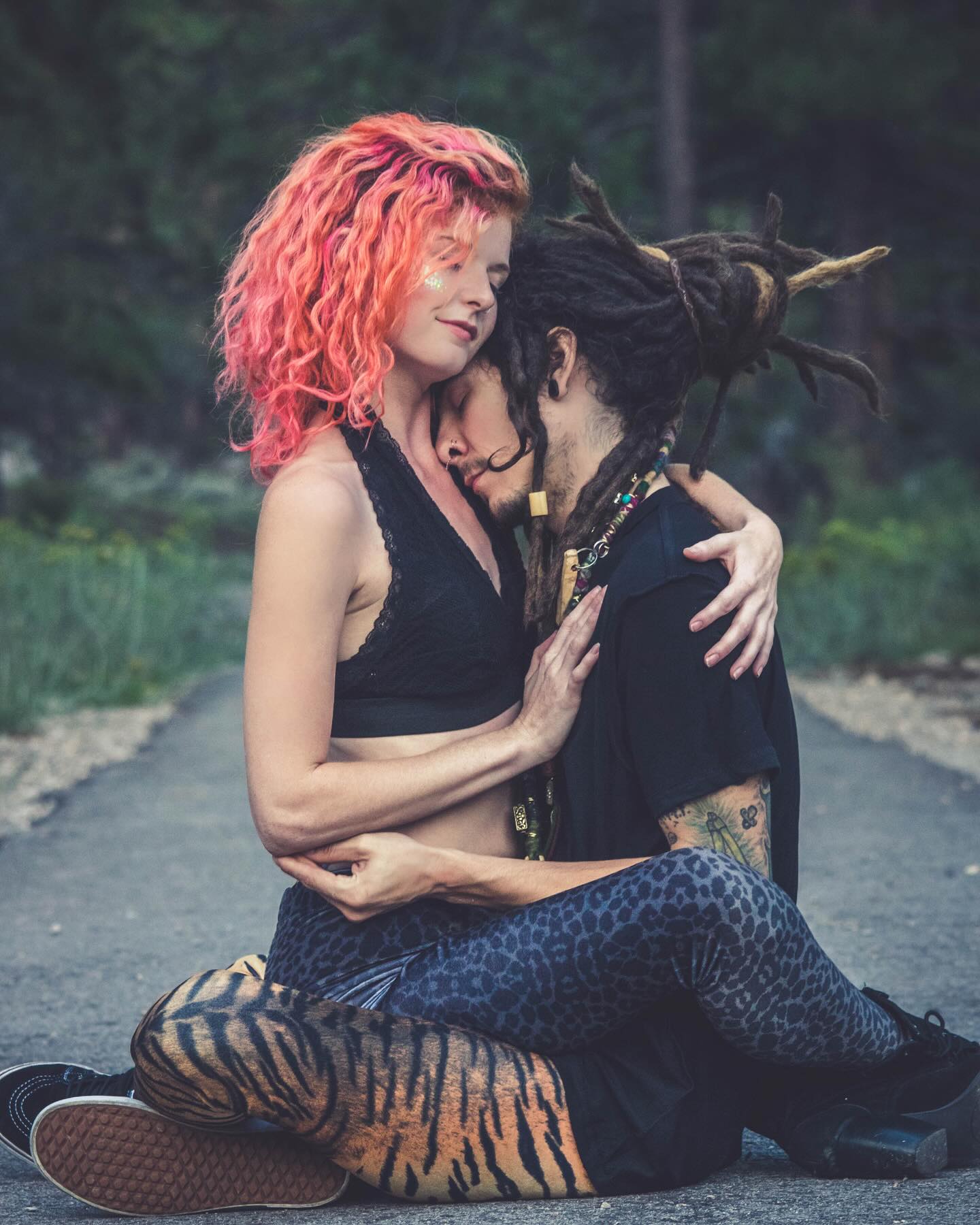 Two people wearing animal print leggings, sitting on a path with one person embracing the other, surrounded by nature.