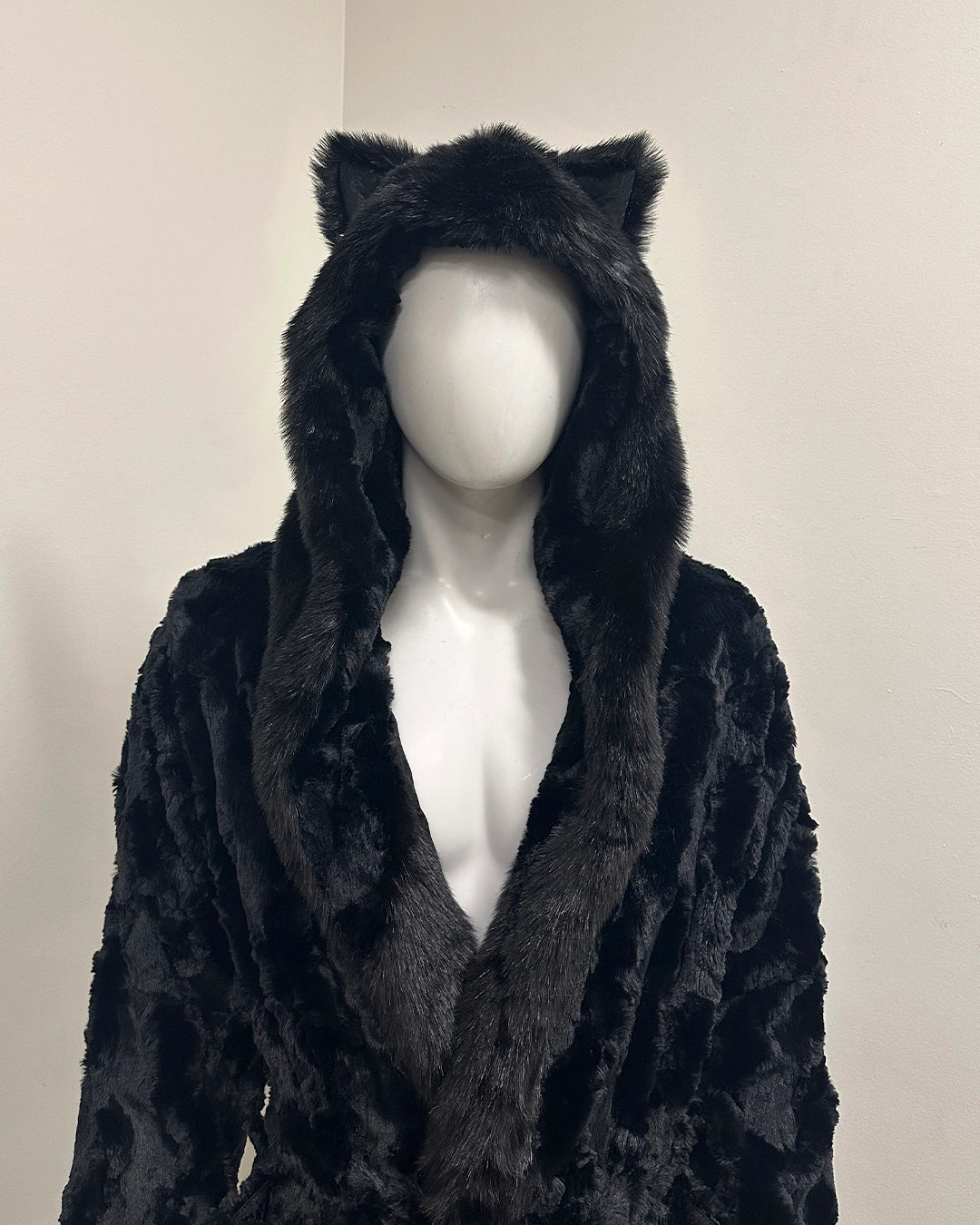 Black faux fur coat with cat ears on a mannequin against a plain background