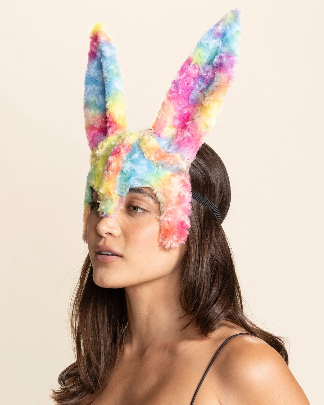 Model wearing a colorful bunny mask in rainbow tie-dye faux fur with large bunny ears against a beige background