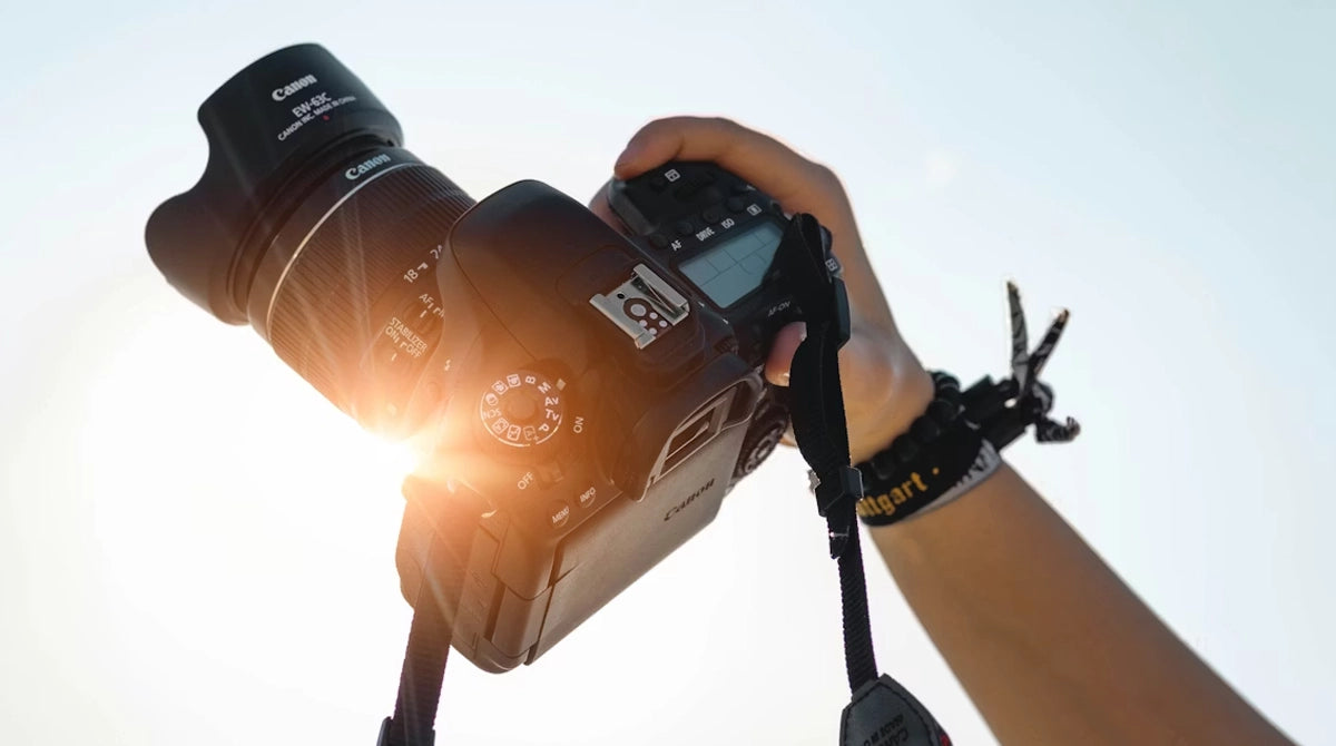 Hand holding a Canon camera with a large lens against a clear sky