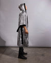 A person wearing a long silver sequin hooded robe with black trim and a black waist tie, standing in profile against a plain light gray studio backdrop.