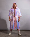 A man wearing a hooded, knee-length iridescent pink and white festival kimono robe with a matching tie belt, standing against a plain gray studio background.