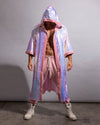 A person modeling a long iridescent holographic hooded kimono robe with pink trim, worn open over pink drawstring pants and white high-top sneakers, against a plain gray studio backdrop.