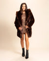 Woman wearing a SpiritHoods brown fake fur coat in plush luxury faux fur over a sparkly dress on a beige background. SpiritHoods Fall Winter Custom Coats and Jackets for Women