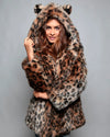 A Woman wearing a leopard print faux fur coat with feline ears a gray background. SpiritHoods Best Selling Leopard Print Coat available in Made To Order, for limited waste.