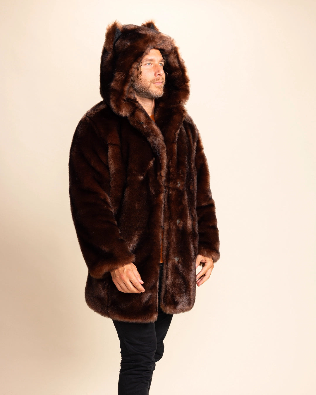 A man wearing a brown faux fur coat with plush over sized hood adorned with wolf ears on a beige background. SpiritHoods made to order faux fur coats and custom made fall winter jackets for men