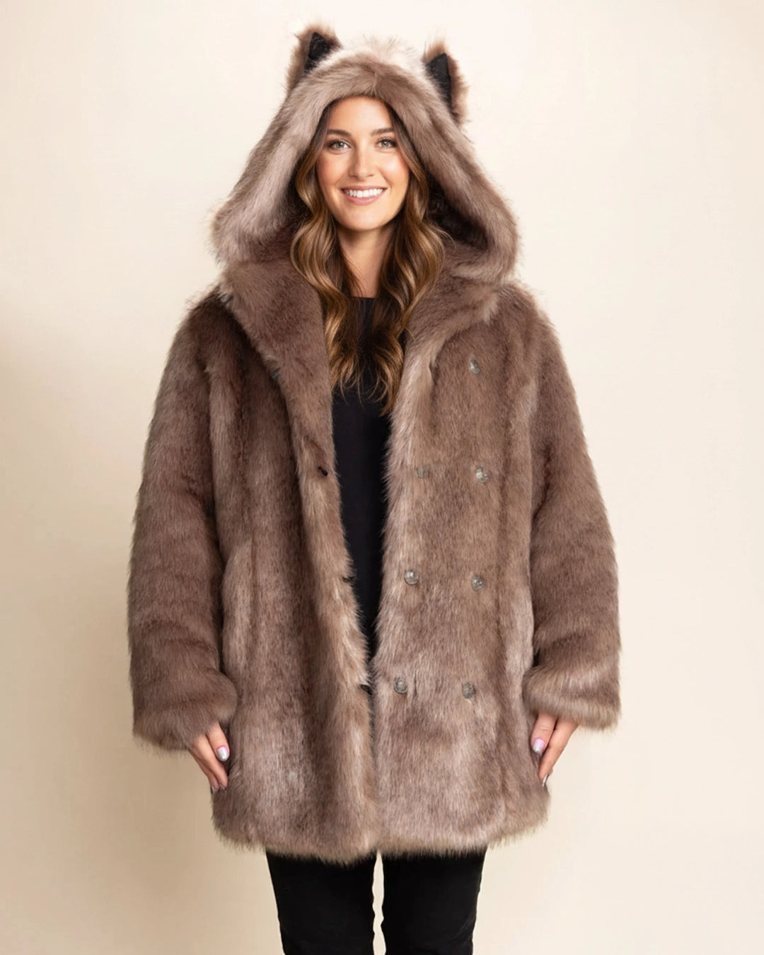Woman smiling at the camera wearing a over-sized brown fake fur coat with a hood  and wolf ears on a beige background. SpiritHoods Italian Wolf Faux Fur Collector Edition Coat for Women