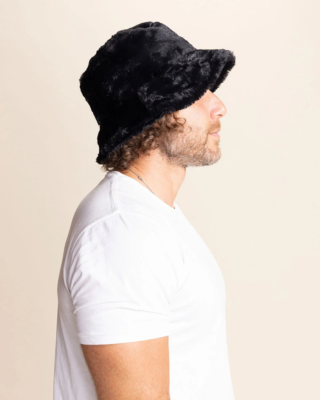 Man wearing a black furry bucket hat against a beige background