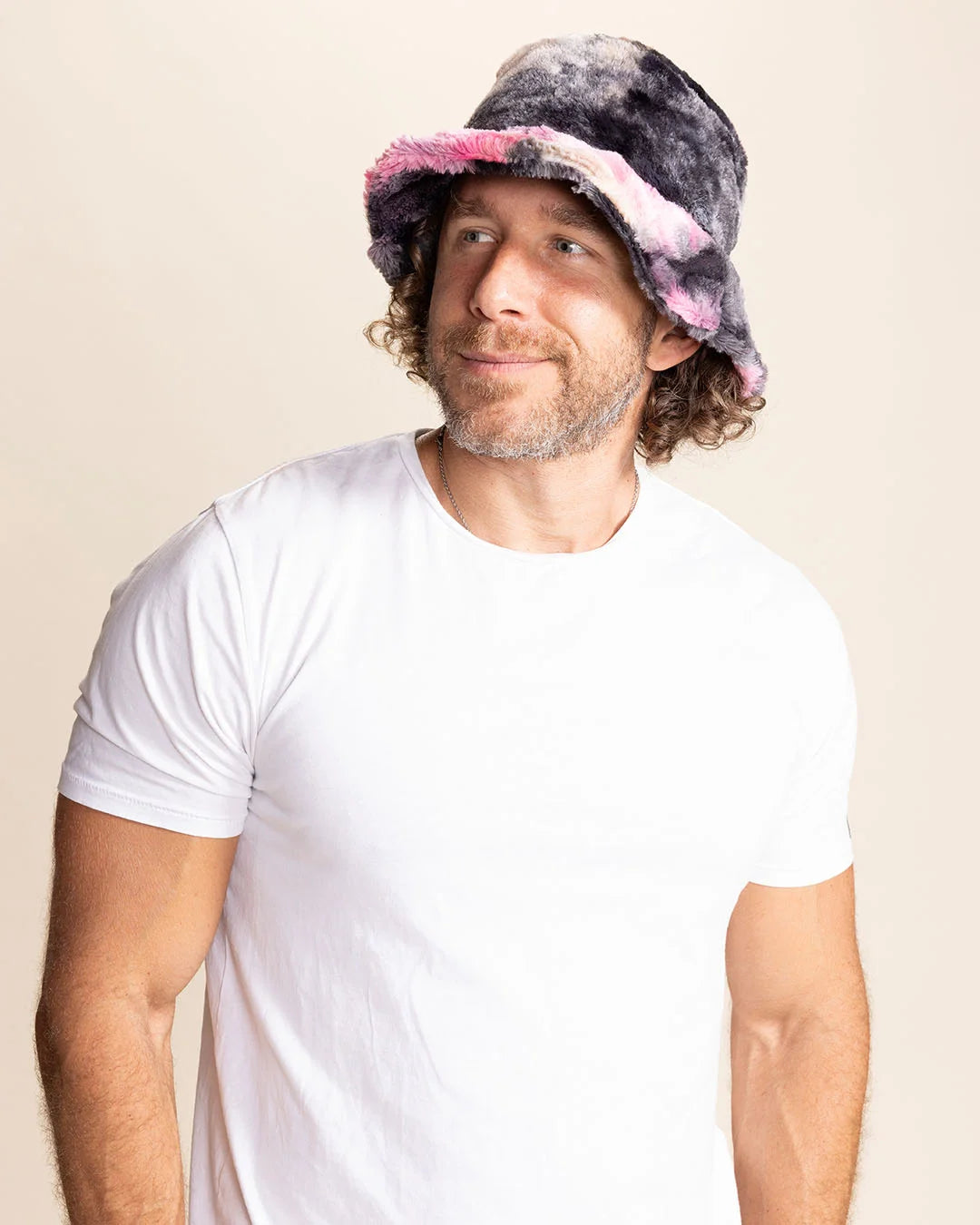 Man wearing a white t-shirt and a colorful tie-dye bucket hat on a beige background