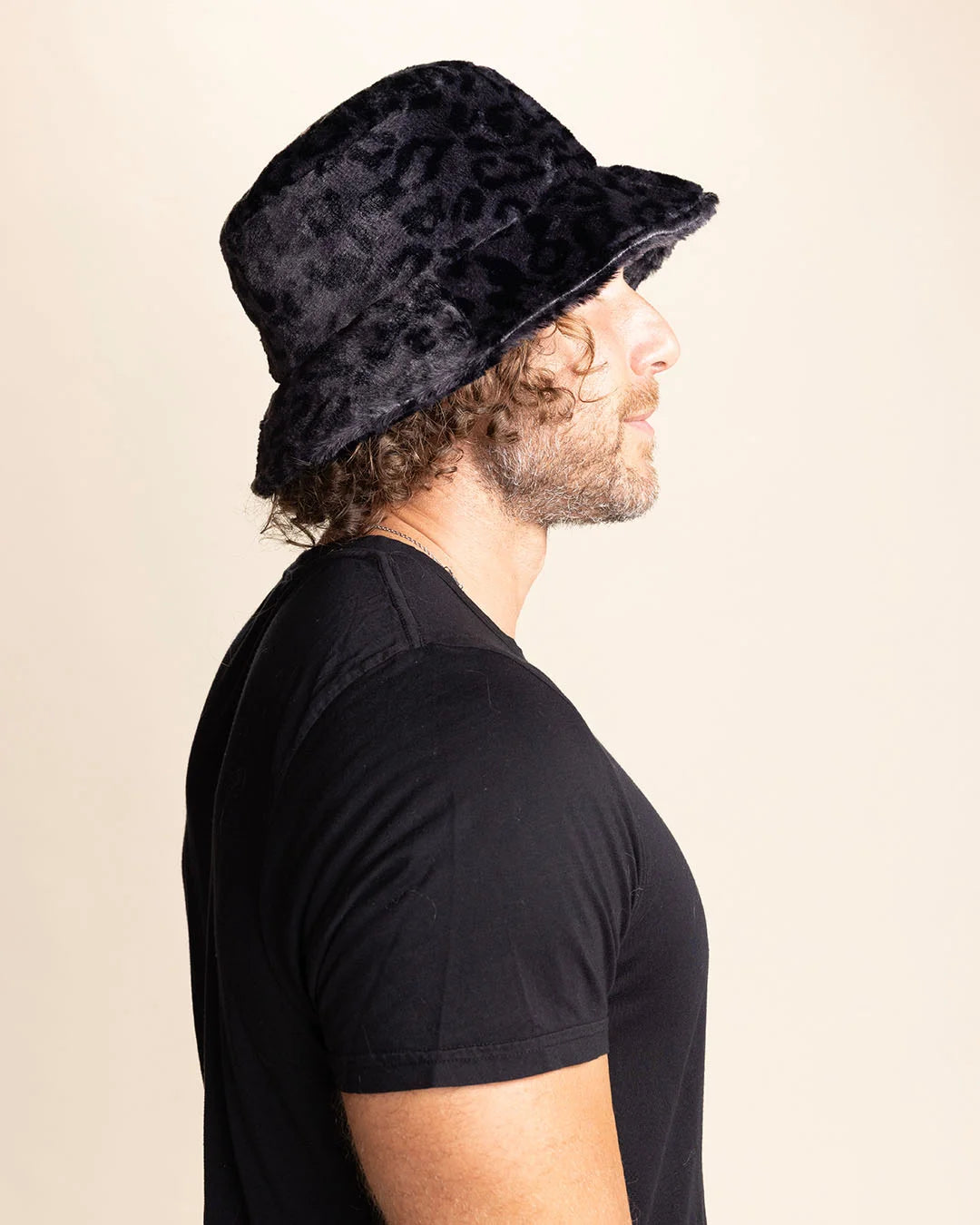A Man wearing a black bucket hat with subtle leopard print pattern on a beige background