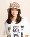 Woman wearing a fuzzy bucket hat and a white t-shirt with cat prints on a beige background