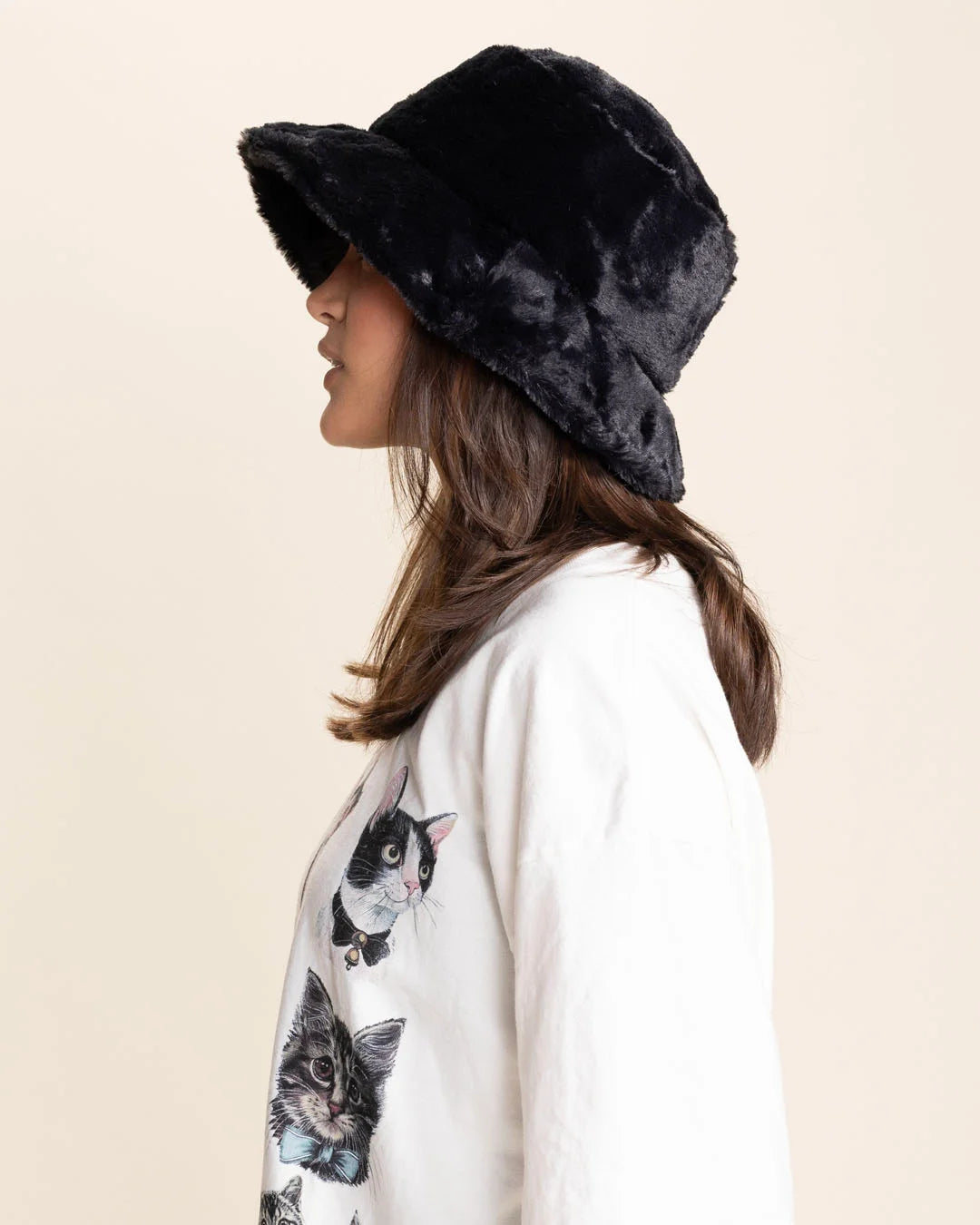 Woman wearing a black bucket hat and a white t-shirt with cat prints on a beige background