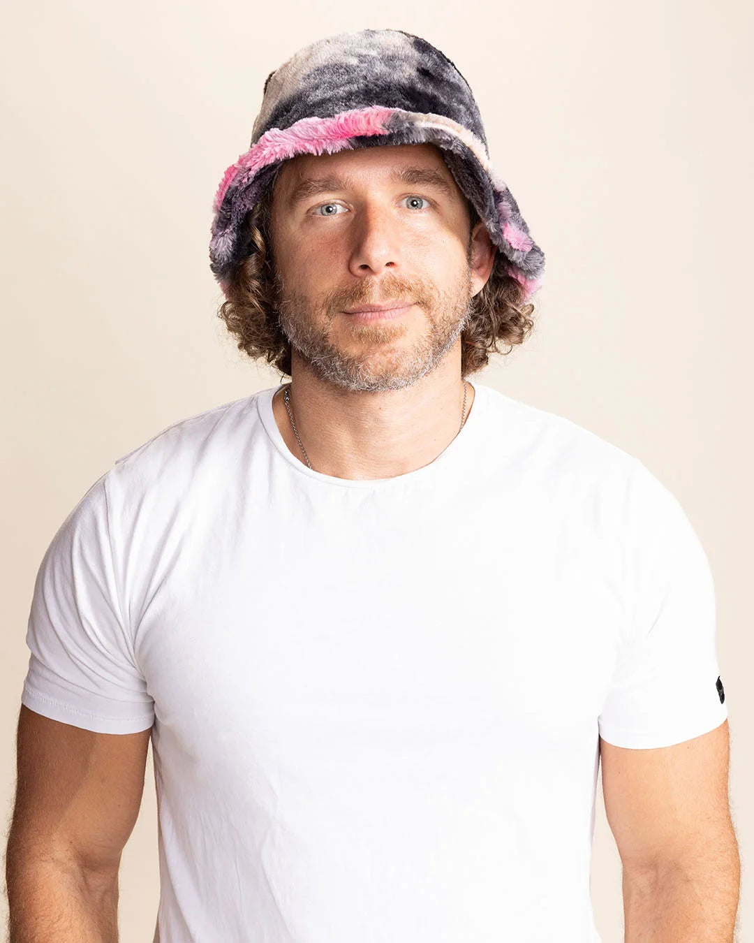 Man wearing a colorful bucket hat against a plain background tie-dye pink black and cream tones.
