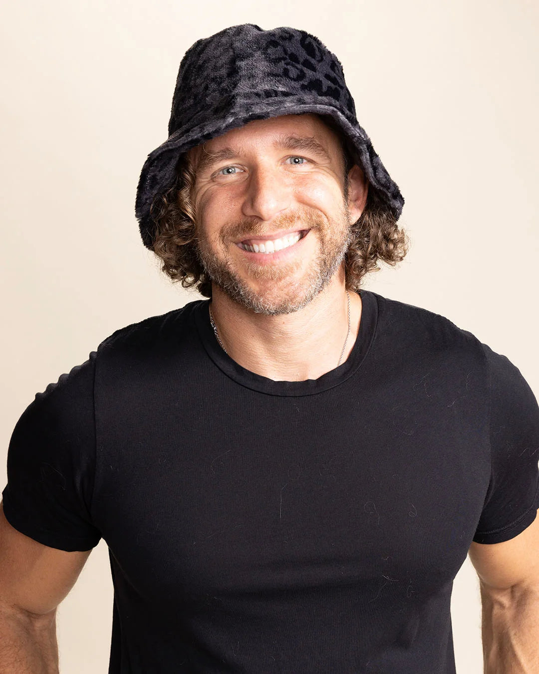A Man wearing a black bucket hat with subtle leopard print pattern on a beige background