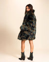 Woman wearing a plush fake fur coat with the collar up, looking over her shoulder smiling, on neutral background. SpiritHoods Fall Winter Coat Collection of Custom Made Fake Fur Jackets.