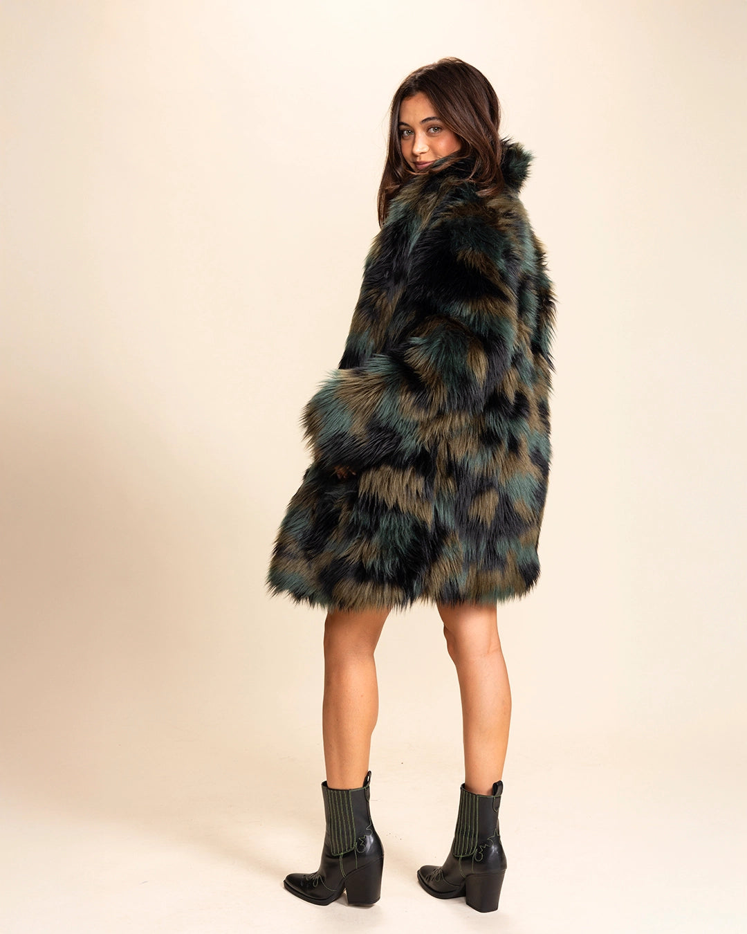Woman wearing a plush fake fur coat with the collar up, looking over her shoulder smiling, on neutral background. SpiritHoods Fall Winter Coat Collection of Custom Made Fake Fur Jackets.