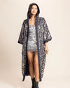 Woman wearing a hooded festival kimono with sparkling silver and gold sequin leopard print over a sequin outfit on a beige background