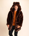 Man wearing a plush brown faux fur coat with wolf ears on a beige background. Wolf face buttons can be seen down the model's side, for easy peacoat button closure. Low-waste production, vegan fashion, peta-approved fake fur coats and jackets.