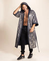 Man wearing a long sequin leopard-patterned kimono over black pants on a beige background