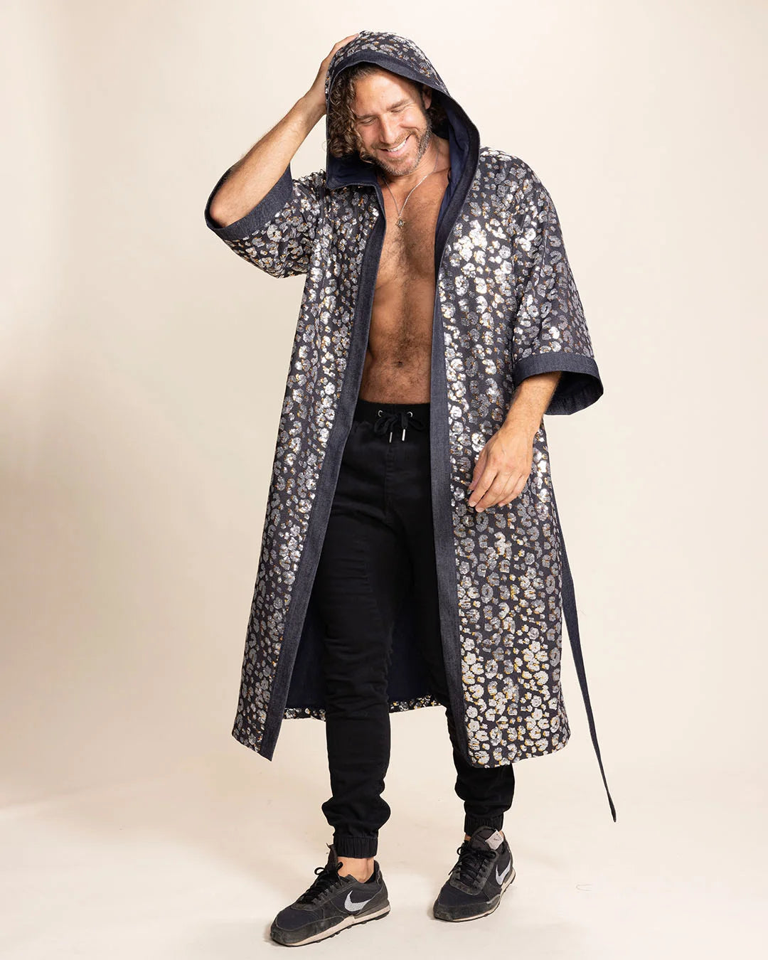 Man wearing a long sequin leopard-patterned kimono over black pants on a beige background