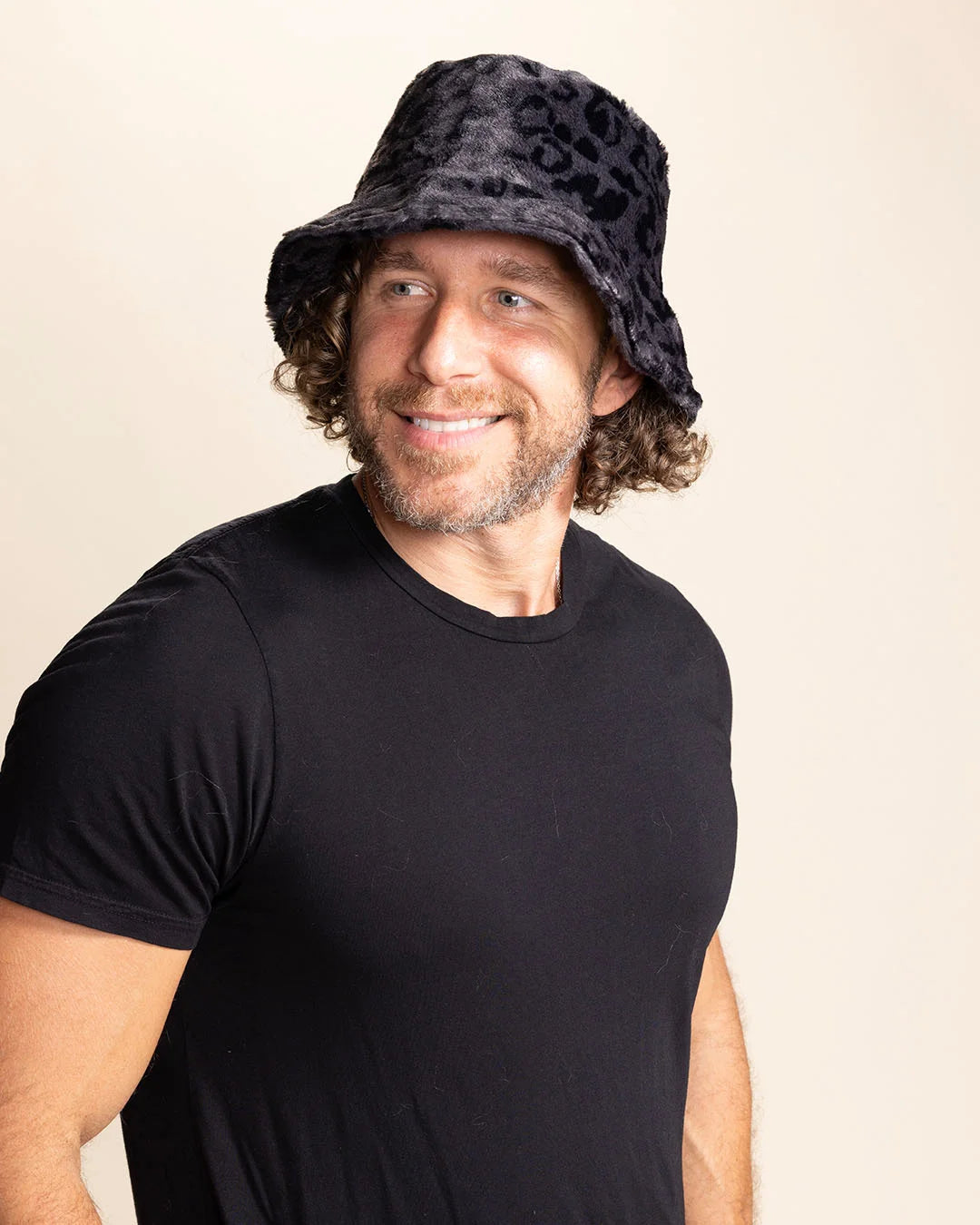 Man wearing a black animal print bucket hat and black t-shirt against a beige background