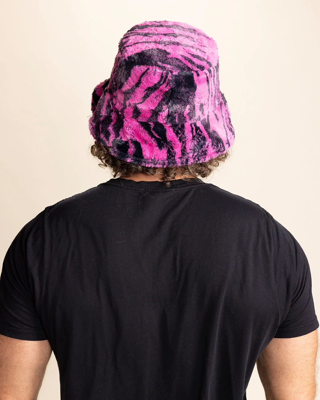 Person wearing a black t-shirt and a pink and black tiger patterned fuzzy bucket hat on a beige background