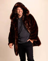 Man wearing a brown fake fur coat against a beige background, smiling wearing a vegan faux fur jacket with hood and peacoat buttons.