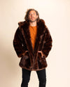 Man wearing a SpiritHoods brown wolf inspired fake fur jacket with the hood down, and his hands in the two outer pockets, against a beige background. SpiritHoods Custom Made Faux Fur Coats and Animal Inspired Jackets.