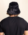 Person wearing a slate grey furry bucket hat with a black leopard pattern on a beige background