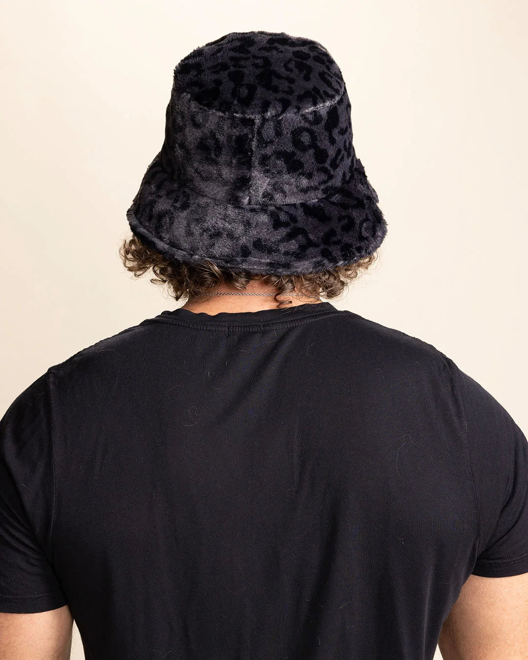 Person wearing a slate grey furry bucket hat with a black leopard pattern on a beige background