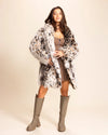 Woman wearing an animal pattern faux fur coat and knee-high boots on a beige background. SpiritHoods Little Cheetah Fake Fur Jacket - Fall Winter Cruelty Free Custom Coat Shop.