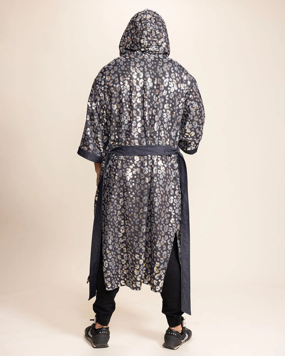 Person wearing a silver sequin leopard-patterned Kimono with hood and belt-tie on a beige background