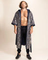 Man wearing a long sequin leopard print robe over black pants on a beige background
