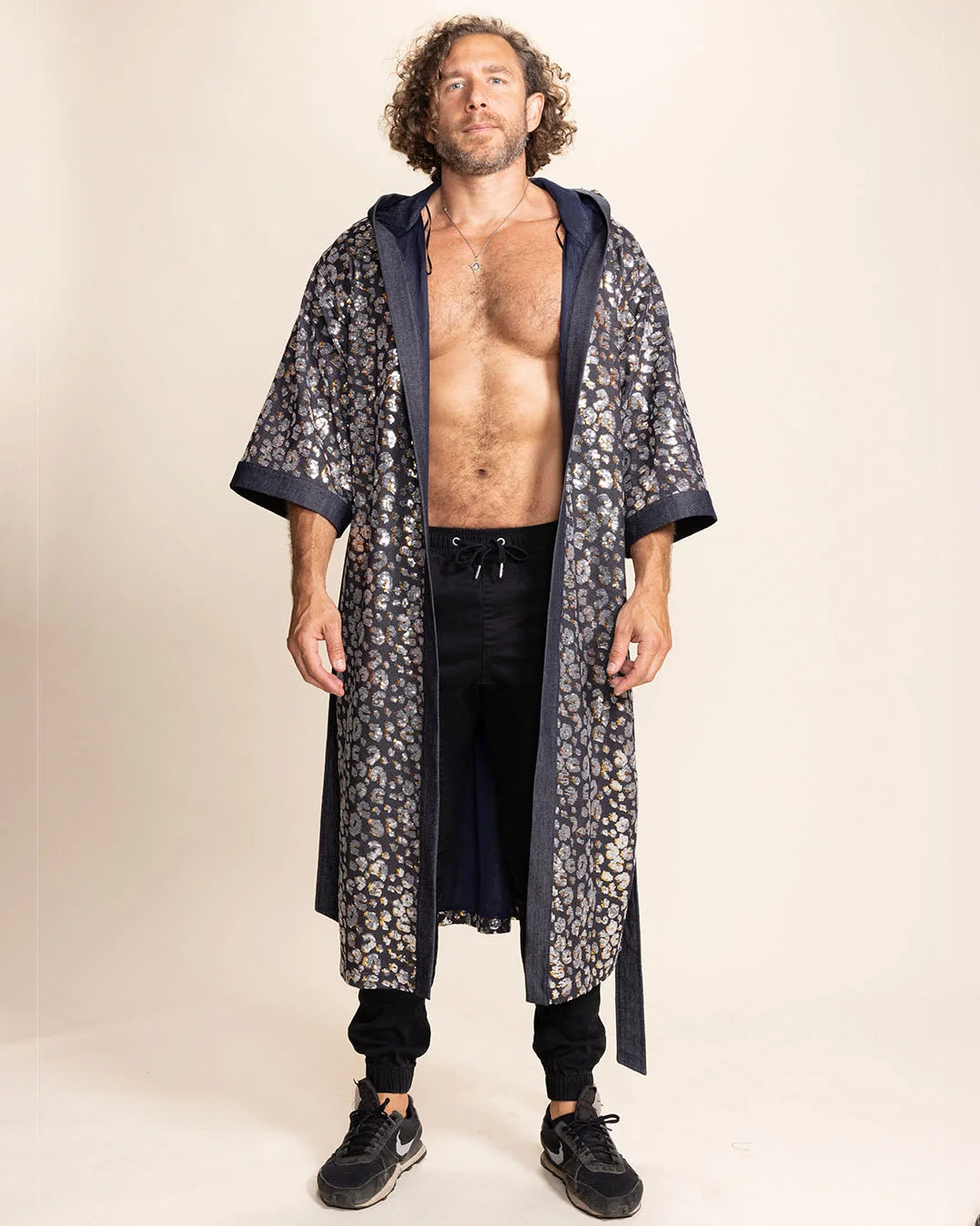 Man wearing a long sequin leopard print robe over black pants on a beige background