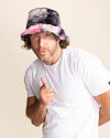 Man wearing a tie-dye bucket hat and giving a thumbs-up gesture on a beige background