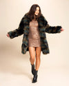 Woman wearing a green, brown, and black tie-dye fake fur coat with the collared down, and her arms out, and dress on a beige background. SpiritHoods Custom Made Fake Fur Jackets.