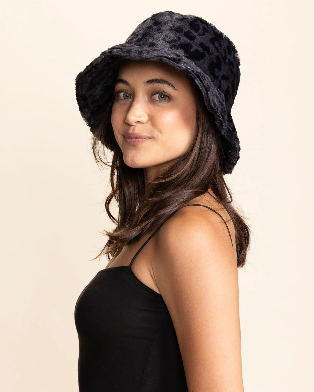 Woman wearing a black furry leopard print bucket hat on a beige background