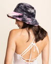 Person wearing a tie-dye bucket hat with pink and gray patterns on a beige background
