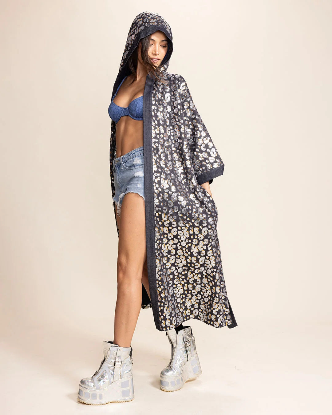 Woman wearing a silver sequin blue denim leopard print kimono with platform shoes against a textured gray wall.