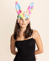 Woman wearing colorful tie-dye bunny ears against a beige background