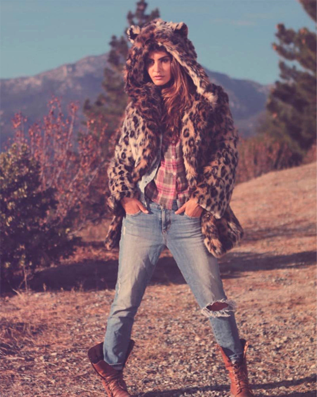 A Woman wearing a leopard print faux fur coat with feline ears a gray background. SpiritHoods Best Selling Leopard Print Coat available in Made To Order, for limited waste.