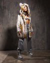 A Woman wearing SpiritHoods White and Gold Classic Arctic Fox Faux Fur Coat over silver pants and platform boots against a textured wall
