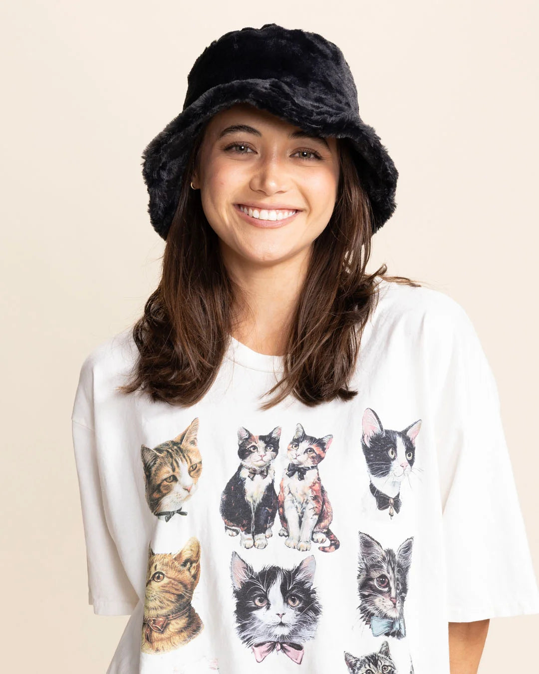 Woman wearing a black bucket hat and a white t-shirt with cat prints on a beige background