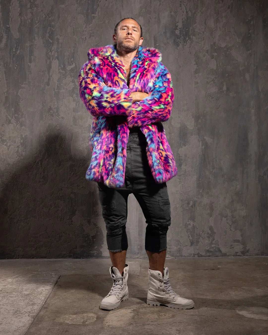 Person wearing a colorful neon leopard print faux fur coat with an oversized hood with ears, against a gray textured wall.